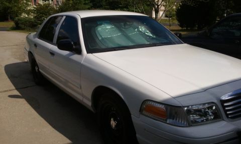 1998 Ford Crown Victoria - A white sedan is parked on a concrete driveway under a bright sky.