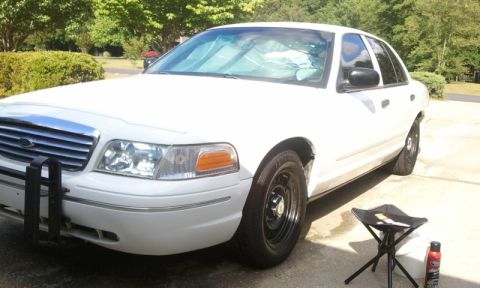 1998 Ford Crown Victoria - Front three-quarter view of a white Ford Crown Victoria sedan sitting in a sunny driveway after a wash, with black steel wheels, chrome bar…