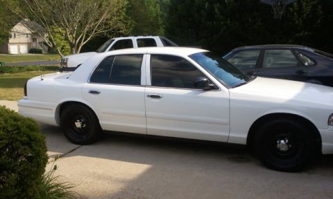 1998 Ford Crown Victoria - Side profile of a white Ford Crown Victoria sedan with tinted windows and black steel wheels, parked on a residential concrete driveway wit…