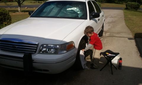 1998 Ford Crown Victoria - Front three-quarter view of a freshly polished white Ford Crown Victoria in a driveway, with a child in a red shirt wiping the front fender…