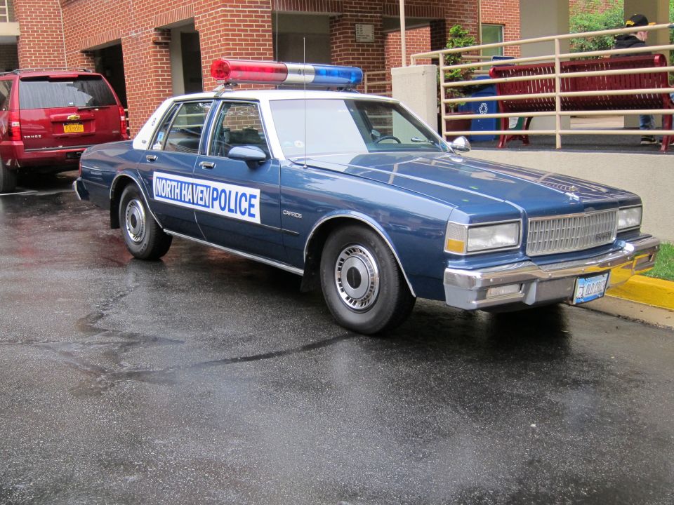 Blue Chevrolet Caprice 'North Haven Police' sedan with light bar parked outside a brick building