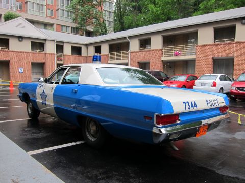1991 Ford LTD Crown Victoria - Rear three-quarter view of a blue and white vintage police sedan marked '7344 POLICE' with a star emblem, parked in a wet apartment lot.