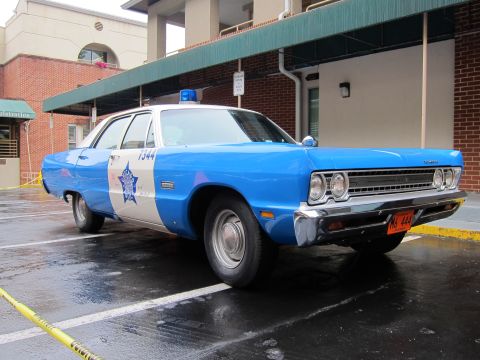 1991 Ford LTD Crown Victoria - blue and white vintage police sedan numbered 1344 with a star emblem and roof light sits on wet pavement beside a covered building entrance.