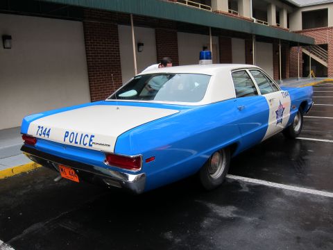 1991 Ford LTD Crown Victoria - Rear three-quarter view of a blue and white vintage police sedan marked '7344 POLICE' parked in a brick courtyard lot, with a person at the…