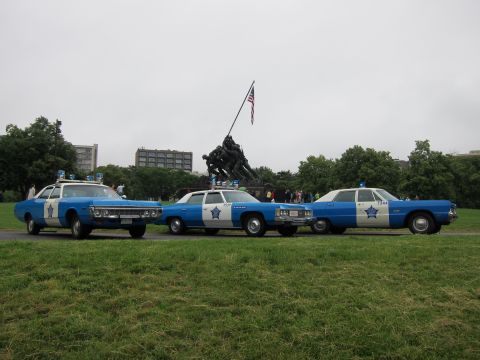1991 Ford LTD Crown Victoria - Three blue-and-white classic police cruisers with star emblems parked on grass in front of the Iwo Jima Memorial.