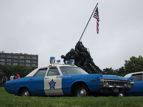 1991 Ford LTD Crown Victoria - blue-and-white police sedan marked 8208 with a star emblem parked on grass before the bronze Iwo Jima Memorial statue.