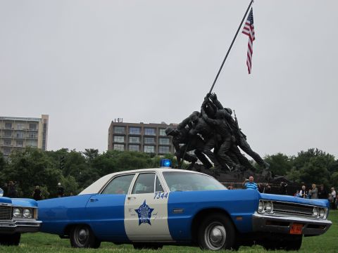 1991 Ford LTD Crown Victoria - blue-and-white classic police sedan marked 7344 parked on grass with the Iwo Jima Memorial statue and a crowd behind it.