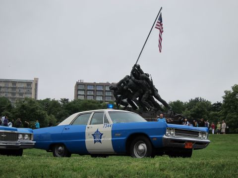 1991 Ford LTD Crown Victoria - blue-and-white classic police car marked 7344 parked on grass before the Iwo Jima Memorial as a crowd gathers nearby.