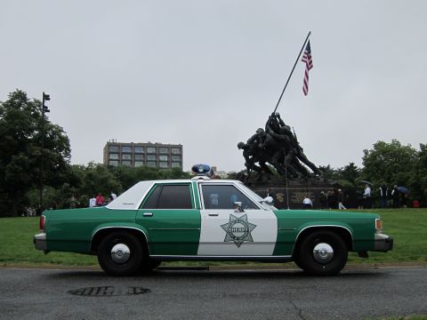 1991 Ford LTD Crown Victoria - green-and-white sheriff sedan bearing a star badge parked on a road before the Iwo Jima Memorial statue.