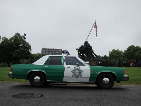 1991 Ford LTD Crown Victoria - Side view of a green-and-white sheriff sedan with a star badge and roof lights parked before the Iwo Jima Memorial.