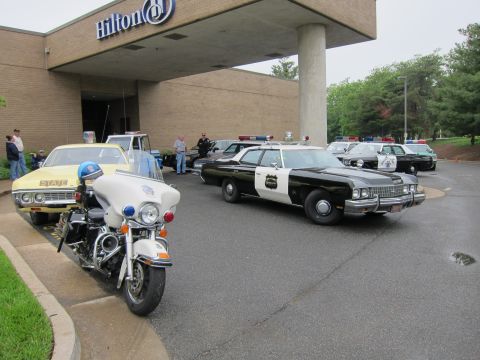 1991 Ford LTD Crown Victoria - black-and-white classic police cruiser and a white patrol motorcycle parked under the Hilton hotel entrance canopy.