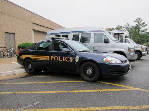 1991 Ford LTD Crown Victoria - dark-blue Chevrolet Impala police sedan with an orange stripe and POLICE lettering parked beside vans in a lot.