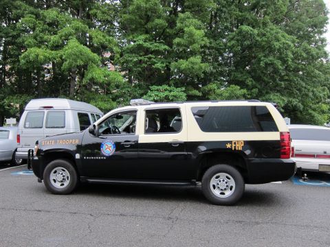 1991 Ford LTD Crown Victoria - Side view of a black-and-tan Chevrolet Suburban marked State Trooper and FHP parked in a wooded lot.