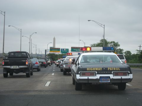 1991 Ford LTD Crown Victoria - vintage Dodge marked HIGHWAY PATROL drives on a busy freeway with the Washington Monument visible in the gray distance.