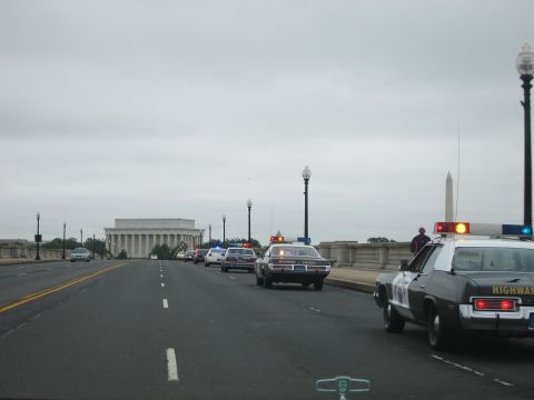 1991 Ford LTD Crown Victoria - line of police cruisers, lead one marked HIGHWAY, crosses a bridge with the Lincoln Memorial and Washington Monument behind.
