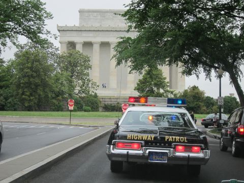 1991 Ford LTD Crown Victoria - rear of a black-and-white Dodge marked HIGHWAY PATROL is parked on a street beneath the columns of the Lincoln Memorial.