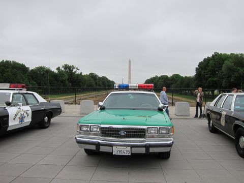 1991 Ford LTD Crown Victoria - green-and-white Ford police sedan sits among parked cruisers as people walk by, the Washington Monument in the background.