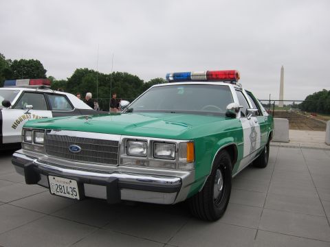 1991 Ford LTD Crown Victoria - green-and-white Ford police sedan with red-and-blue lightbar is parked on a plaza, the Washington Monument in the distance.