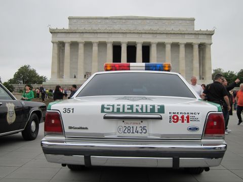 1991 Ford LTD Crown Victoria - white-and-green Ford Crown Victoria marked SHERIFF parks among visitors before the Lincoln Memorial under a gray sky.
