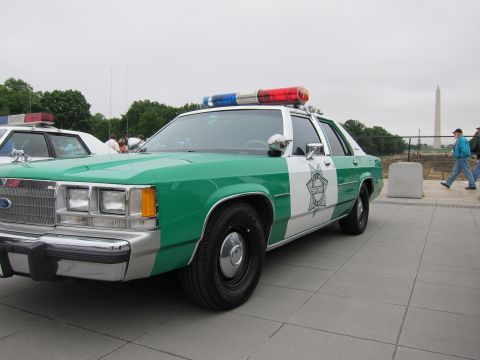 1991 Ford LTD Crown Victoria - green-and-white Ford police sedan with chrome grille and roof lights is parked with the Washington Monument in the distance.