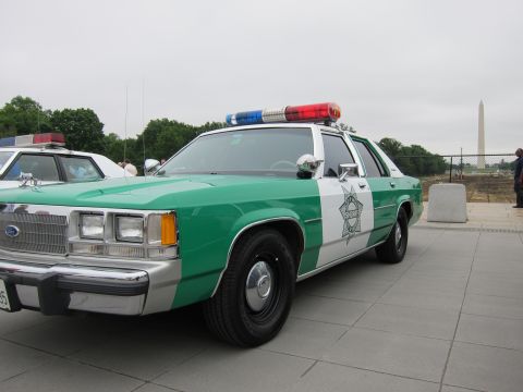 1991 Ford LTD Crown Victoria - green-and-white Ford police sedan with red-and-blue lightbar is parked on a plaza, the Washington Monument behind it.