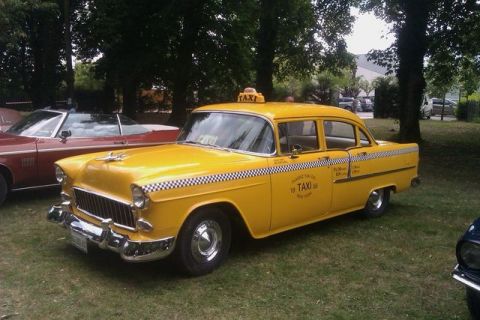 1991 Ford LTD Crown Victoria - A vintage yellow taxi cab is parked on a grassy area, with a red convertible visible to its left.