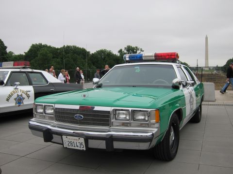 1991 Ford LTD Crown Victoria - green-and-white Ford police sedan with red-and-blue lightbar is parked on a plaza, the Washington Monument in the distance.