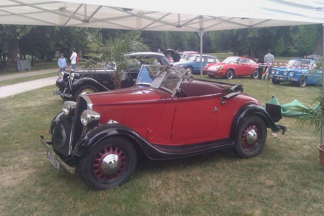 Red convertible with black fenders and wire wheels parked on grass