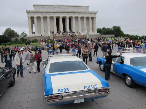 1991 Ford LTD Crown Victoria - vintage blue-and-white police cruiser marked 8208 sits before the Lincoln Memorial as crowds gather on the plaza.