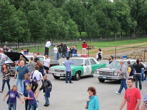 1991 Ford LTD Crown Victoria - Vintage green-and-white and tan police cars on display draw a crowd of spectators on a tree-lined plaza.