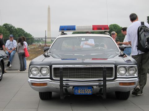 1991 Ford LTD Crown Victoria - Front view of a silver Dodge police cruiser with roof light bar and California plate, the Washington Monument behind it.