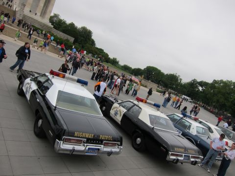 1991 Ford LTD Crown Victoria - Two black-and-white Dodge Highway Patrol cruisers parked at an angle on a plaza with spectators in the background.