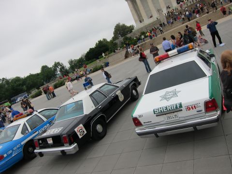 1991 Ford LTD Crown Victoria - green-and-white Ford Sheriff cruiser parked beside a black-and-white police car and a blue NYPD car on a plaza.