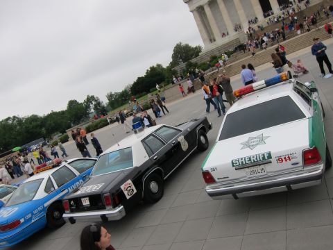 1991 Ford LTD Crown Victoria - row of vintage police cruisers, led by a green-and-white Sheriff Ford, lined up near the steps of the Lincoln Memorial.