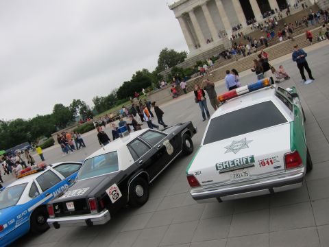 1991 Ford LTD Crown Victoria - Green Sheriff, black-and-white, and blue NYPD vintage cruisers parked before the crowded Lincoln Memorial steps.