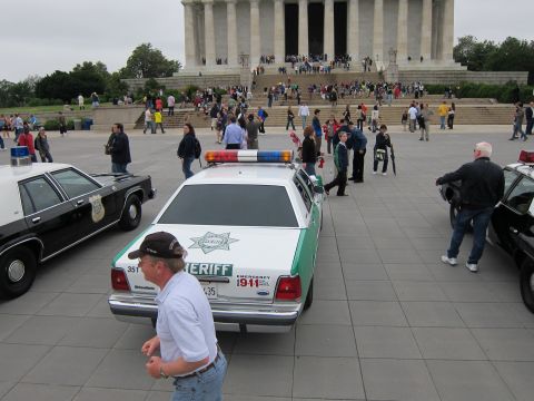 1991 Ford LTD Crown Victoria - green-and-white Sheriff cruiser parked on a plaza with a man walking past and the Lincoln Memorial steps behind.