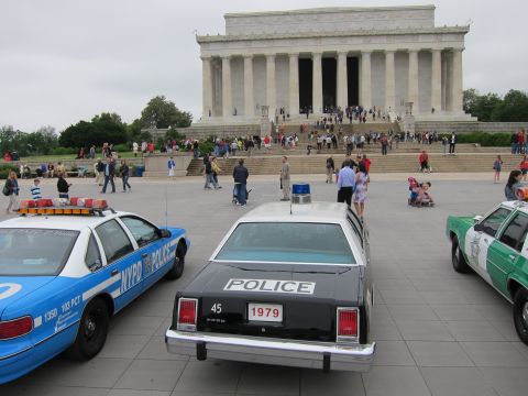 1991 Ford LTD Crown Victoria - black-and-white Ford police car bearing a 1979 plate parked between blue and green cruisers before the Lincoln Memorial.