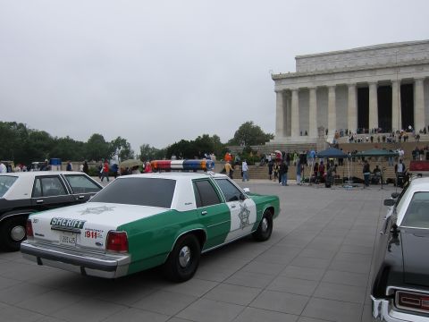1991 Ford LTD Crown Victoria - green-and-white Ford Sheriff cruiser parked among other police cars near the Lincoln Memorial under an overcast sky.