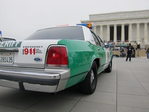 1991 Ford LTD Crown Victoria - Rear view of a green-and-white Ford Sheriff cruiser with light bar parked on a plaza facing the Lincoln Memorial.