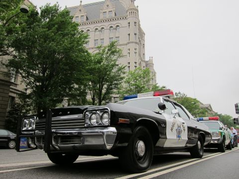 1991 Ford LTD Crown Victoria - Low-angle front view of a black-and-white police sedan with chrome push bar and star decal parked near a tall stone clock tower.