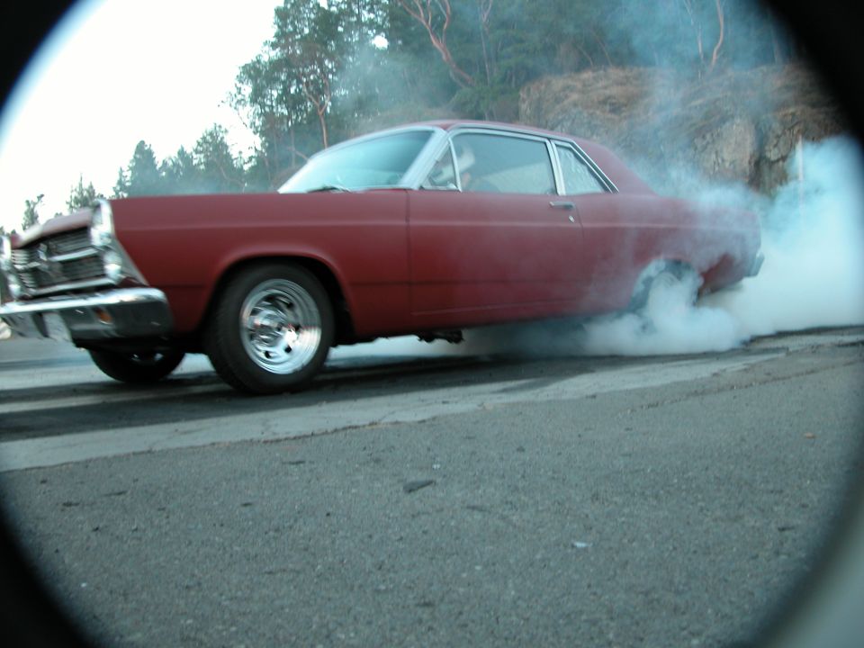 Red two-door coupe doing a smoky burnout on pavement, shot through a circular vignette