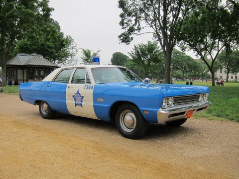 1991 Ford LTD Crown Victoria - blue-and-white classic police sedan with a six-point star decal numbered 7344 parked on a gravel path in a tree-lined park.