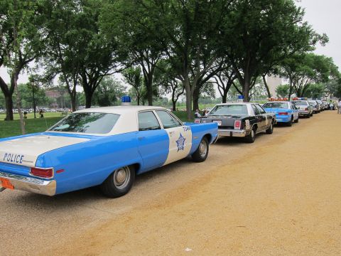1991 Ford LTD Crown Victoria - line of vintage police cars parked along a gravel park path, led by a blue-and-white Chicago Police sedan.