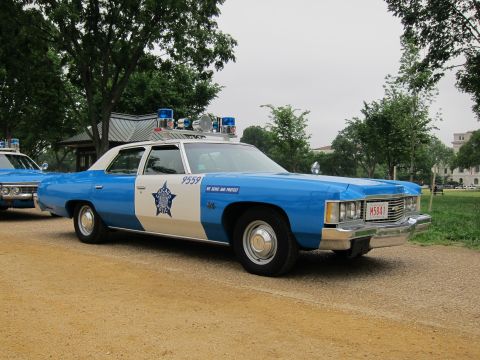 1991 Ford LTD Crown Victoria - blue-and-white Chicago Police full-size sedan with twin roof beacons and a star badge, parked on gravel in a park.