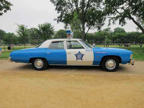 1991 Ford LTD Crown Victoria - blue-and-white Chicago Police full-size sedan numbered 9559 with 'We Serve and Protect' lettering, shown in side profile.