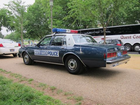 1991 Ford LTD Crown Victoria - dark blue 'North Haven Police' sedan with a light bar, shown in rear three-quarter view next to a tour bus.