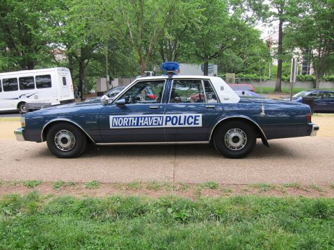 1991 Ford LTD Crown Victoria - dark blue 'North Haven Police' sedan numbered 8 with a roof beacon, shown in side profile near a white van.
