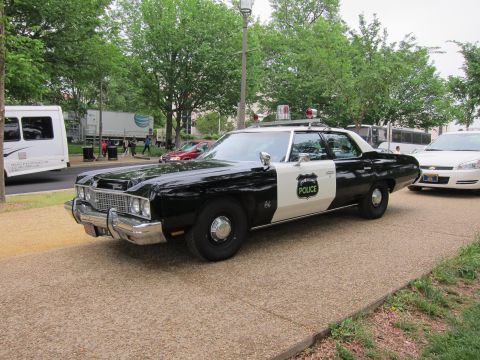 1991 Ford LTD Crown Victoria - black-and-white police sedan with a 'Police' star badge and twin roof beacons, parked on a paved park path.
