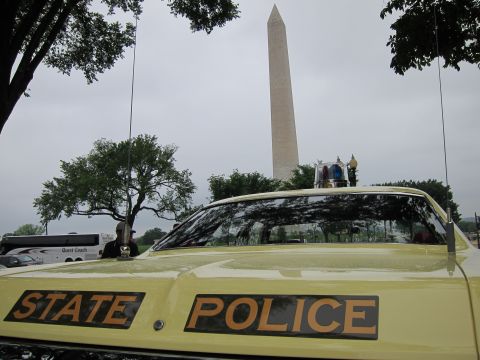 1991 Ford LTD Crown Victoria - Gold STATE POLICE lettering and twin antennas on a yellow car's trunk, with the Washington Monument in the distance.