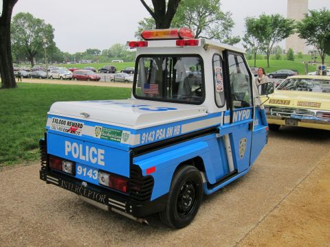 1991 Ford LTD Crown Victoria - small blue-and-white three-wheeled NYPD parking enforcement vehicle marked POLICE 9143 sits on a paved path in a park.
